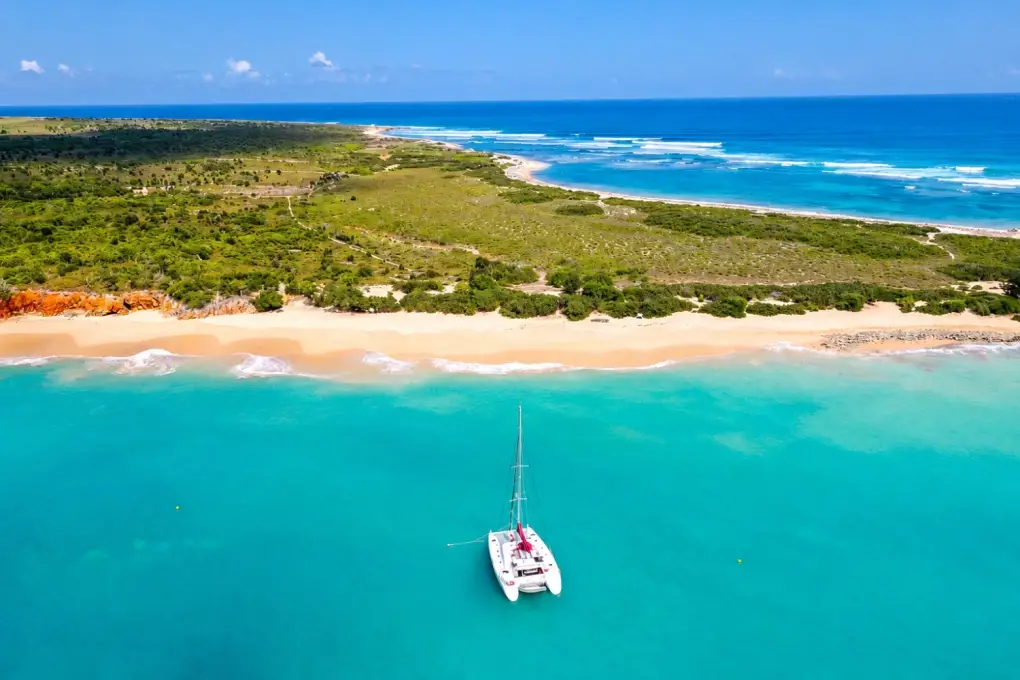 Aerial view of a catamaran anchored in turquoise ocean water off the white sand beach of Tintamarre Island, Saint Martin.